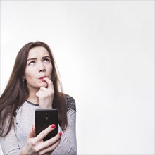 Thoughtful young woman holding her mobile phone with her fingers mouth