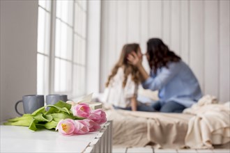 Tulip flowers table near bed with hugging mother daughter
