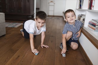 Two boys playing with car toys hardwood floor