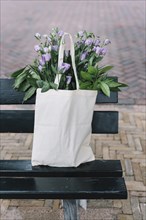White cotton handbag with beautiful purple eustoma flowers black bench