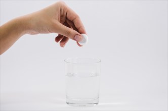 Woman s hand holding white pill glass water against grey backdrop