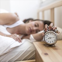 Woman sleeping bed turning off alarm clock