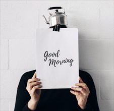 Woman with kettle head good morning message paper holding front face against white wall