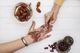 Artist making mehndi womans hand near dates fruit