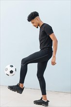Black sportsman kicking football blue wall background