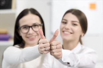 Blurred young businesswomen showing thumb up sign toward camera