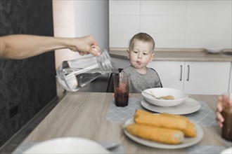 Boy looking person pouring water glass breakfast