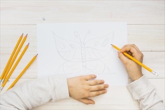 Child hand sketching butterfly with pencil wooden background