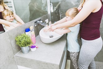Crop mother helping daughter wash hands