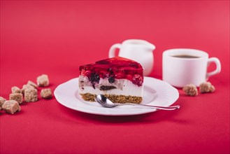 Delicious strawberry jelly cheese cake white plate with brown sugar cubes against red backdrop