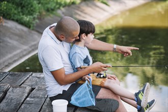 Fisherman showing something his son while fishing lake