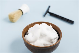 Foam wooden bowl front razor shaving brush against blue background
