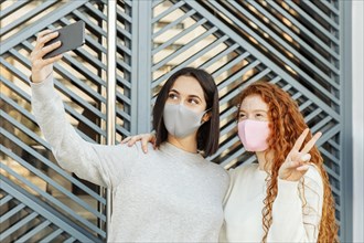 Front view female friends with face masks outdoors taking selfie