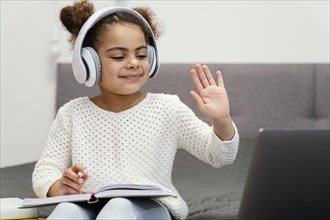 Front view little girl waving using laptop online school