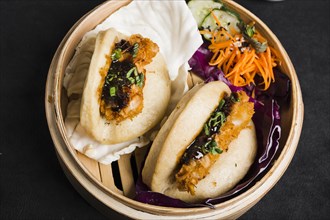 Gua bao steamed buns with salad inside bamboo steamer black background