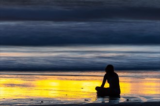Woman meditating at sunset on sandy beach