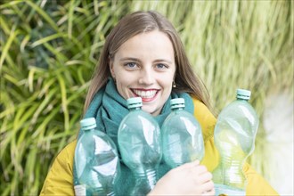 Young woman with plastic bottles in front of plant wall as environmental protection
