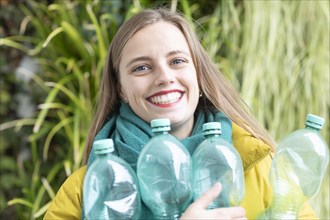 Young woman with plastic bottles in front of plant wall as environmental protection