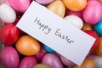 Happy Easter written on a small piece of paper on colorful decorative rocks in display