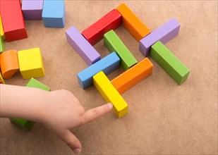 Toddler hand over Colorful building blocks on brown background