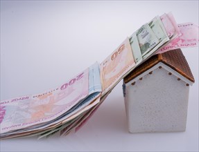Turkish Lira banknotes on the roof of a model house on white background