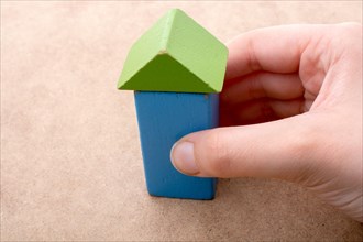 Hand holding a house formed out of building blocks s on a brown background
