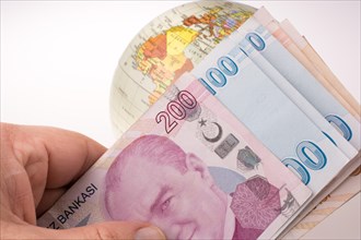 Hand holding Turkish Lira banknotes by the side of a model globe on white background