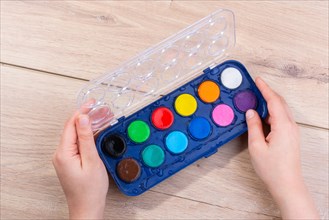 Hand holding a watercolor paint box on a wooden background