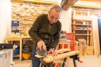 Carpenter using an electric tool to polish a piece of wood in studio workshop