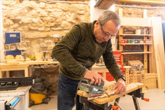 Mature artisan polishing a piece of wood using an electric tool in a workshop