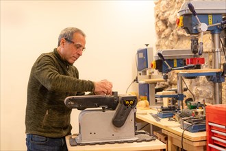 Man using a machine to sand a piece of wood in an artisan workshop