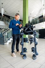 Mechanical exoskeleton computer engineer looking at the robot with a tablet. Physiotherapy in a modern hospital: Robotic skeleton. Physiotherapy Rehabilitation Scientists