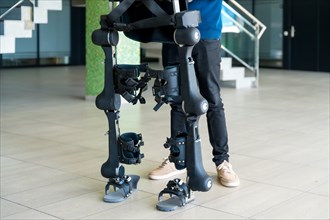Unrecognizable computer engineer in mechanical exoskeleton looking at the robot with a tablet. Physiotherapy in a modern hospital: Robotic skeleton. Physiotherapy Rehabilitation Scientists