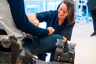 Mechanical exoskeleton. Physiotherapy smiling in modern hospital: Female physiotherapist helping disabled person with robotic skeleton with tapes. Futuristic rehabilitation