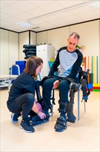 Mechanical exoskeleton. Physiotherapy in a modern hospital: Female physiotherapist helping disabled person with robotic skeleton with tapes. Futuristic rehabilitation