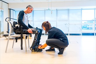 Mechanical exoskeleton. Physiotherapy in a modern hospital: Female physiotherapist placing tapes on disabled person with robotic skeleton. Futuristic rehabilitation