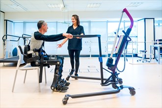 Mechanical exoskeleton. Physiotherapy assistant lifting disabled person with robotic skeleton to get up. Futuristic rehabilitation