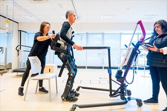 Mechanical exoskeleton. Physiotherapy medical assistant lifting disabled person with robotic skeleton to get up. Futuristic rehabilitation