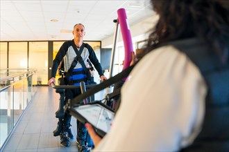 Mechanical exoskeleton. Physiotherapy woman helping disabled person to walk with robotic skeleton. Futuristic rehabilitation