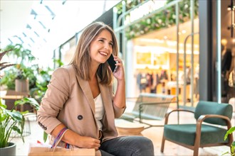 Woman talking to the phone sitting on a department store carrying shopping bags