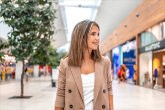Woman walking along a indoor shopping mall with trees and shops inside