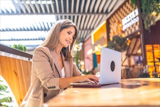 Side view of a cheerful elegant businesswoman using laptop sitting on a cafeteria