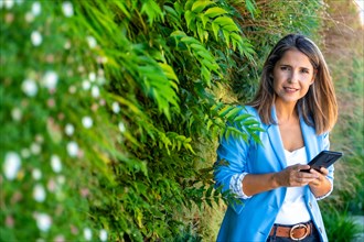 Casual businesswoman using phone next to trees and bushes in an urban park