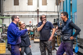 Team of workers laughing at the job of a metal industrial factory in the numerical control sector talking