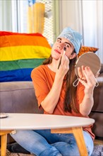 Vertical photo of a gay person making up at home next to a rainbow lgbt flag