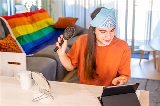 Transgender person brushing the long hair while using tablet sitting on the living room