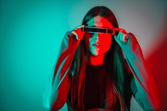 Futuristic studio portrait with neon lights of a transgender person with long hair using smart googles