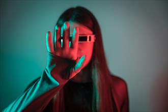 Futuristic studio portrait with neon lights of a transgender person gesturing while using augmented reality smart goggles
