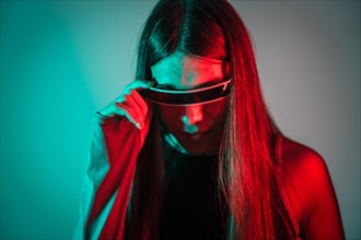 Studio portrait with neon lights of a curious futuristic transgender person using smart goggles