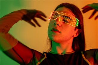 Futuristic studio portrait with neon lights of a sensual non-binary person gesturing while using virtual reality goggles